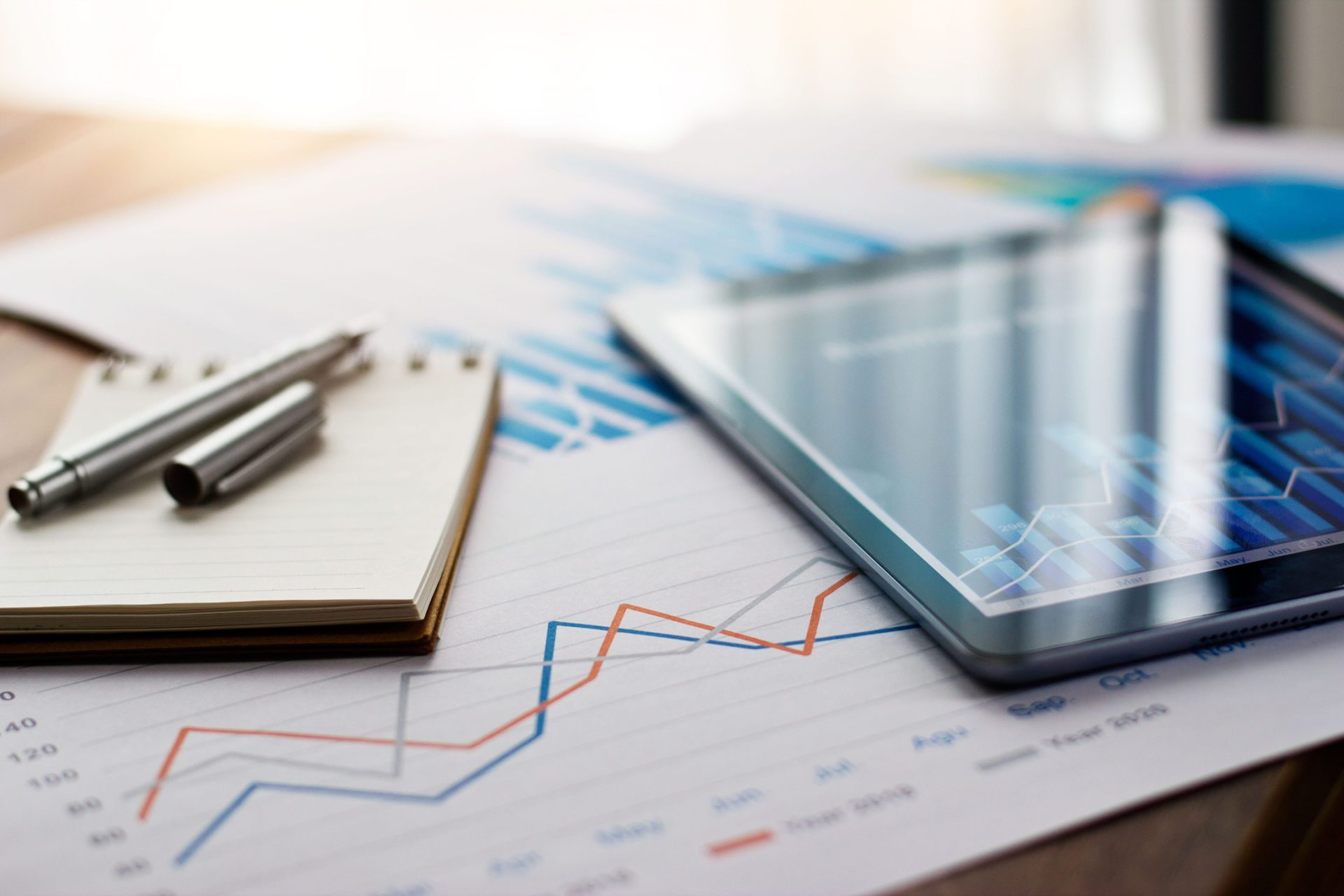 Image of a tablet and paperwork with graphs